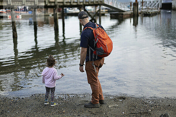 Vater und junge Tochter stehen am Ufer eines Strandes und blicken auf den Hafen von Horseshoe Bay in BC  Kanada; West Vancouver  British Columbia  Kanada