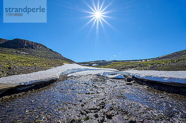 Gebirgsbach mit Schneefeld und Sonnenaufgang bei strahlend blauem Himmel im Sommer  Hellisheidi Eystri Bergpass in Nordisland; Ketilsstadhir  Austurland  Island