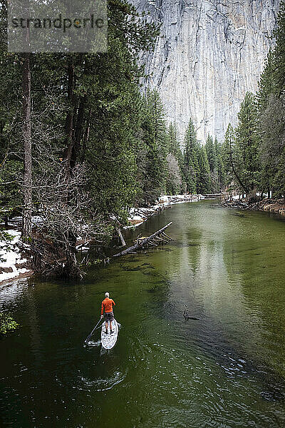 Standup Paddleboarding auf einem ruhigen Fluss mit einer steilen Klippe und Wald vor sich