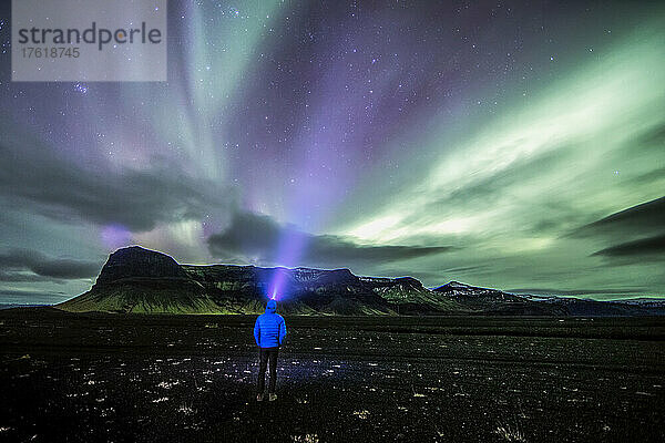 Ein Mann geht in einer abgelegenen Region Islands auf eine entfernte Bergwut zu.
