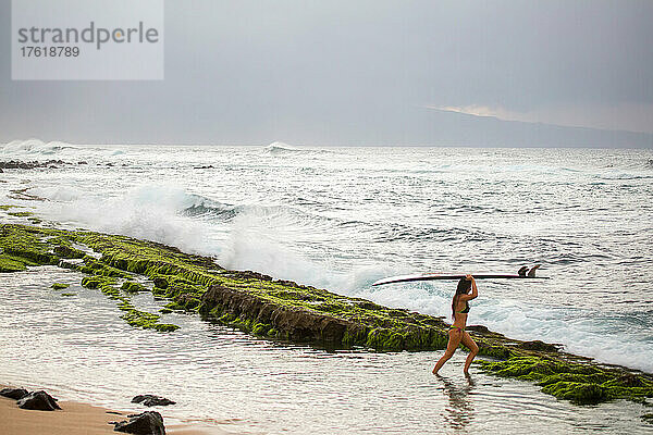Eine Profi-Surferin trägt ihr Surfbrett auf die Wellen hinaus.