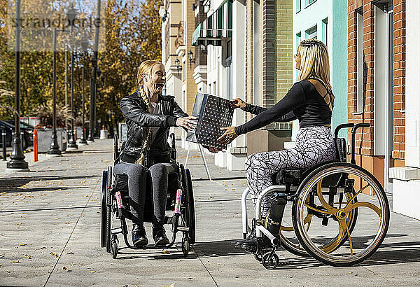 Zwei junge  querschnittsgelähmte Frauen in ihren Rollstühlen besuchen an einem schönen Herbsttag gemeinsam einen Gehweg  wobei die eine der anderen ein Geschenk überreicht; Edmonton  Alberta  Kanada