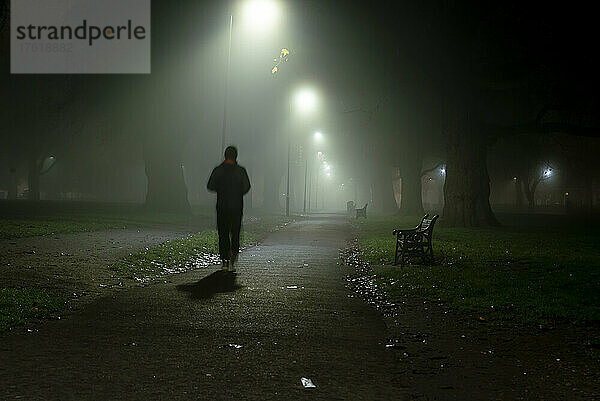 Bewegungsunschärfe und Silhouette einer Person  die an einem nebligen Morgen in London Fields  Shoreditch  London  UK  spazieren geht; London  England