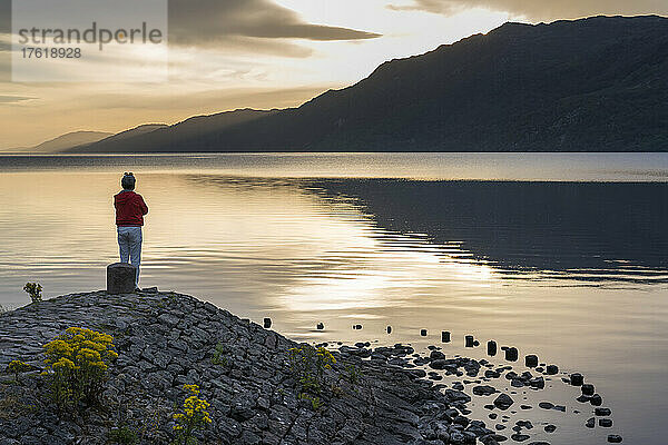Bei Sonnenaufgang blickt ein Mann auf das ruhige Wasser des Loch Ness in Schottland; Fort Augustus  Schottland