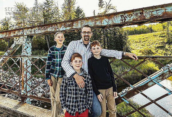 Außenporträt eines Vaters mit drei Söhnen  die auf einer Brücke in einem Park stehen; Edmonton  Alberta  Kanada