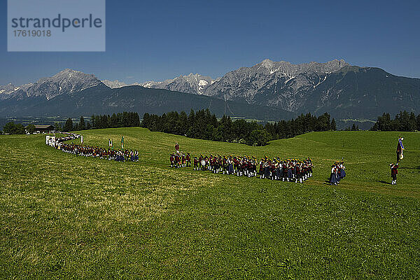 Der Festzug zum Herz-Jesu-Fest zieht in eine große Wiese ein  die vom Karwendelgebirge überragt wird; Österreich.