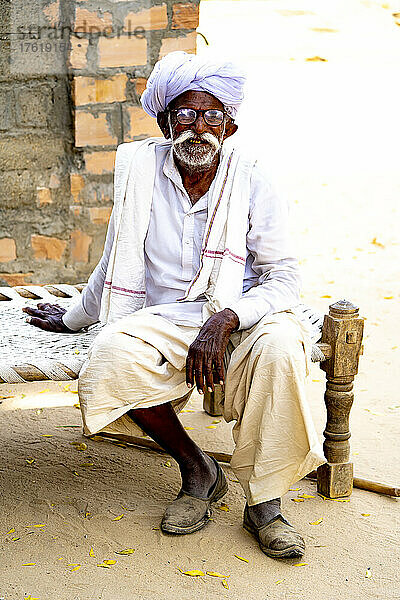 Alter Mann mit weißem Turban und Schnurrbart  der auf einem Bett aus Charpoy im Dorf Bishoi sitzt; Bezirk Pali  Rajasthan  Indien