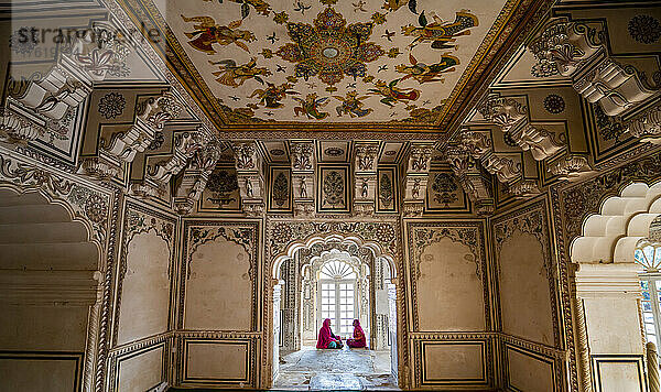 Frauen sitzen in einer Fensternische einer bemalten Halle im Ahhichatragarh Fort; Nagaur  Rajasthan  Indien