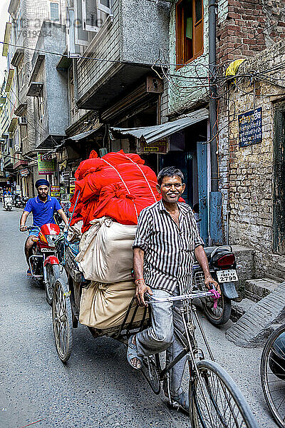 Ein Mann fährt auf einem Fahrrad und zieht einen beladenen Anhänger hinter sich her  während ein Mann auf einem Motorrad auf einer Straße in Indien folgt; Amritsar  Punjab  Indien