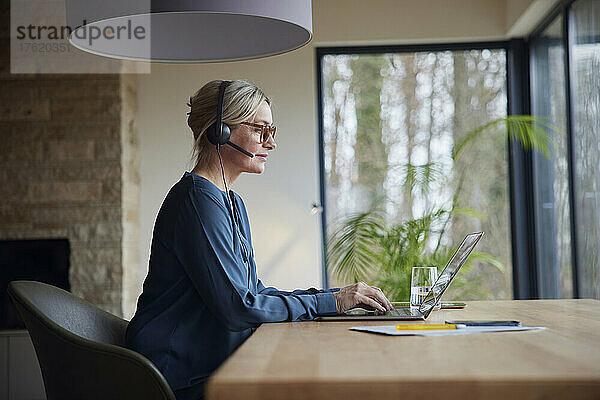 Blonde Frau mit Kopfhörern und Laptop am Tisch sitzend