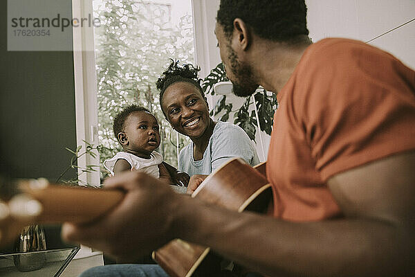 Father plucking guitar by son and mother in living room