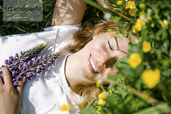 Happy woman with eyes closed lying on grass on sunny day