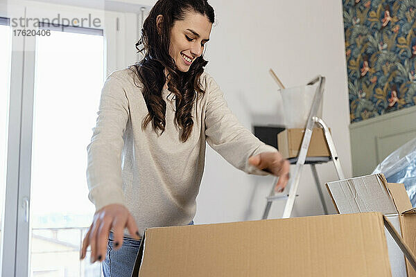 Lächelnde Frau packt Kartons aus und zieht in ein neues Zuhause