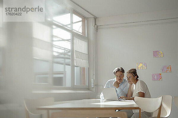 Geschäftsmann und Geschäftsfrau sitzen mit Laptop und diskutieren am Schreibtisch im Büro