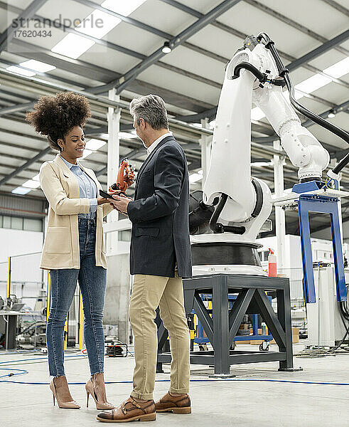 Techniker zeigt Modell eines Roboterarms und diskutiert mit Geschäftsmann in Fabrik
