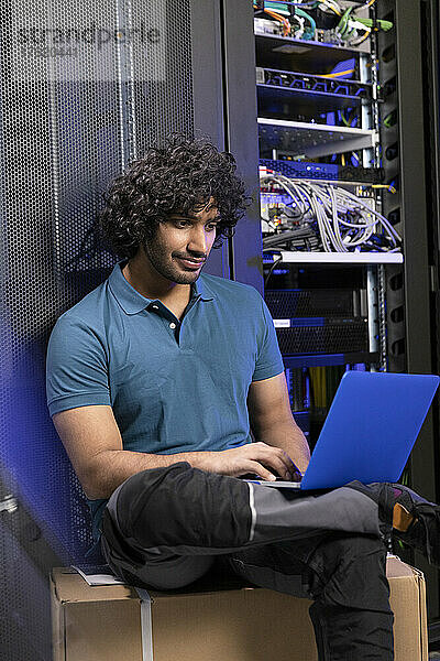 Computerprogrammierer sitzt mit Laptop auf einer Kiste im Serverraum