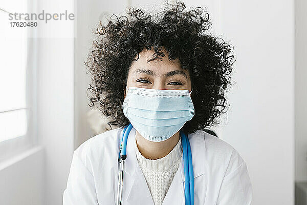 Junger Arzt mit lockigem Haar trägt schützende Gesichtsmaske in der medizinischen Klinik