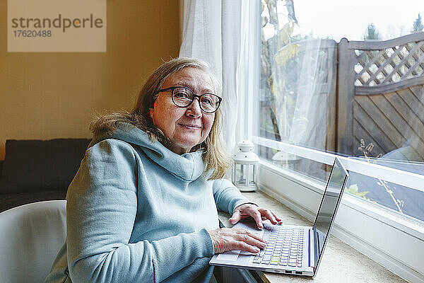 Ältere Frau benutzt Laptop am Fenster zu Hause