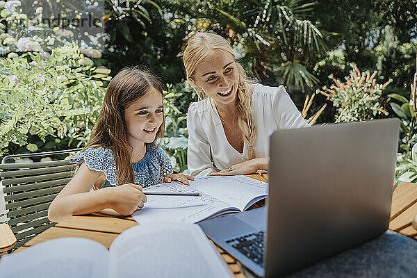 Lächelnde Mutter und Tochter im Online-Unterricht über Laptop im Hinterhof