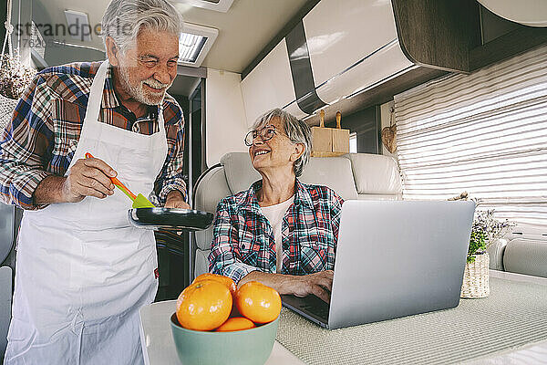 Smiling senior woman looking at man with cooking pan at motor home