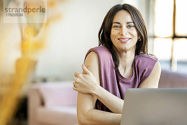 Lächelnde Geschäftsfrau mit Laptop sitzt zu Hause