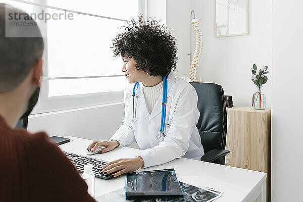 Junger Arzt sitzt am Computer und sitzt mit Patient in der Klinik