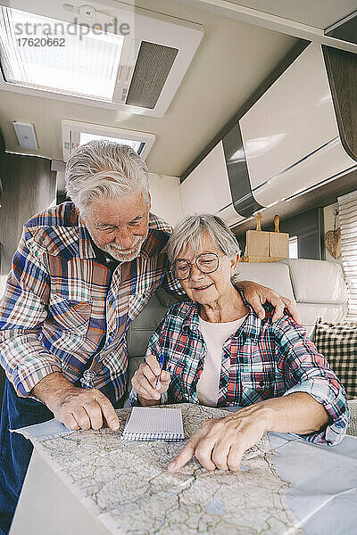 Lächelndes älteres Paar diskutiert im Wohnmobil über Reiseführerkarte