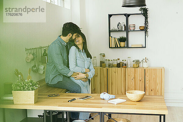 Lächelndes junges Paar  das sich zu Hause in der Küche umarmt