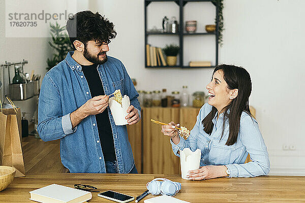 Lächelnde Frau und Mann essen Nudeln mit Stäbchen in der heimischen Küche