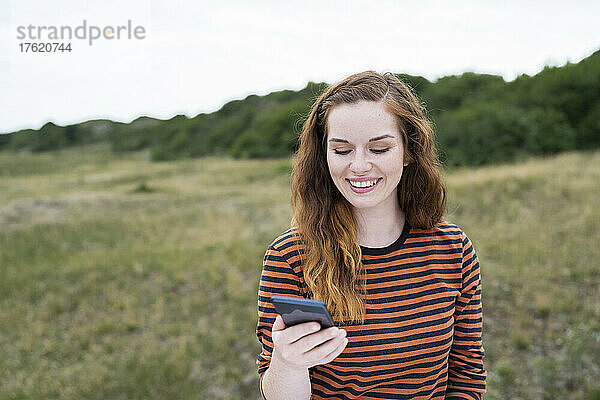 Lächelnde rothaarige Frau benutzt Smartphone auf der Wiese