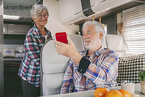 Älterer Mann zeigt lächelnder Frau im Wohnmobil Smartphone