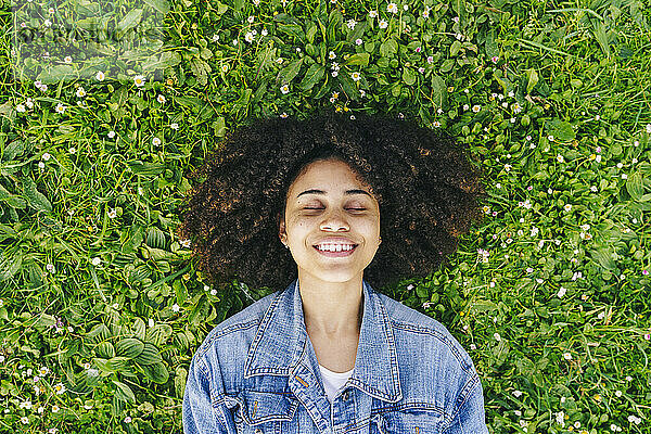 Smiling Afro woman lying on green flowering plants on meadow