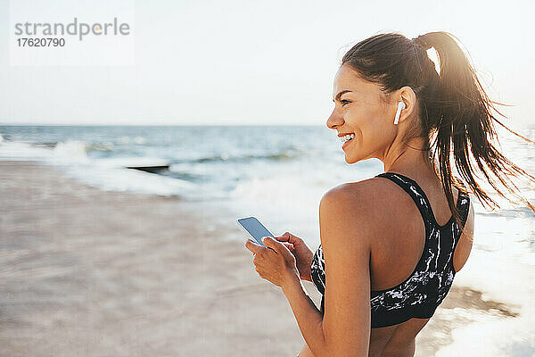 Glückliche junge Frau mit Smartphone am Strand