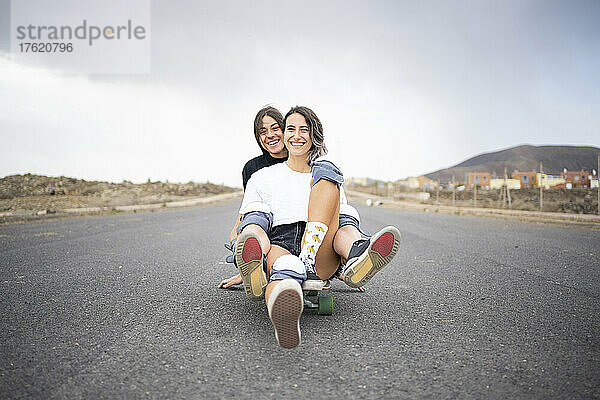 Glückliche Freunde sitzen zusammen auf dem Skateboard