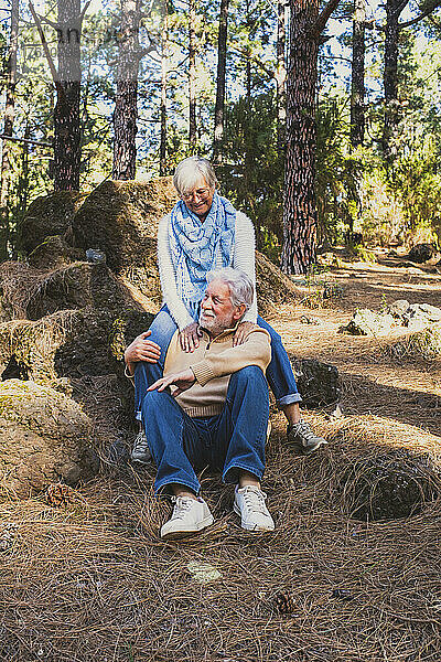 Glückliches älteres Paar sitzt auf Felsen im Wald