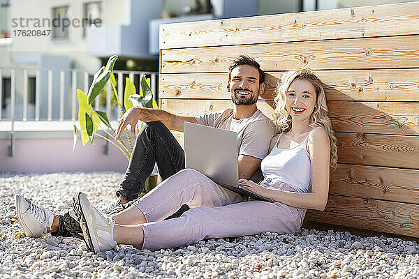 Glückliches junges Paar sitzt an einem sonnigen Tag mit Laptop