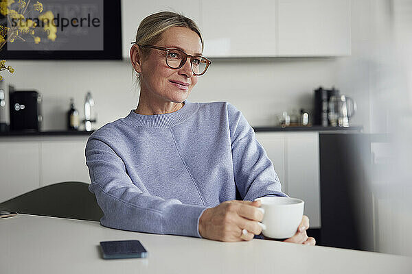 Geschäftsfrau mit Brille und Kaffeetasse sitzt am Tisch