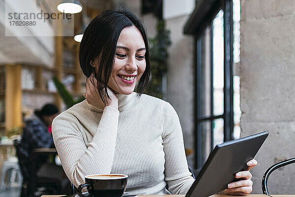 Lächelnde Frau mit Tablet-PC sitzt im Café