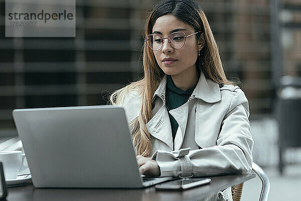 Freiberufler mit Brille und Laptop im Straßencafé