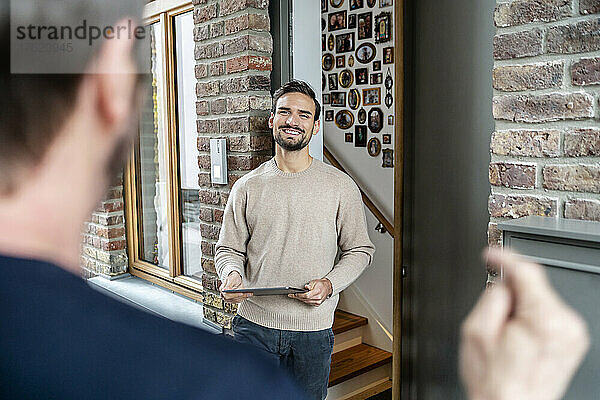 Lächelnder Mann hält Tablet-PC im Gespräch mit Freund vor dem Haus