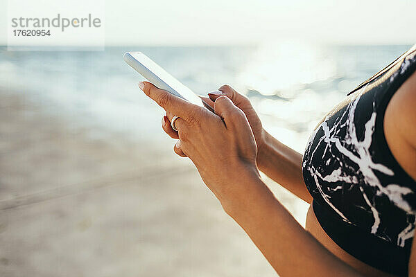 Frau im Sport-BH benutzt Smartphone am Strand