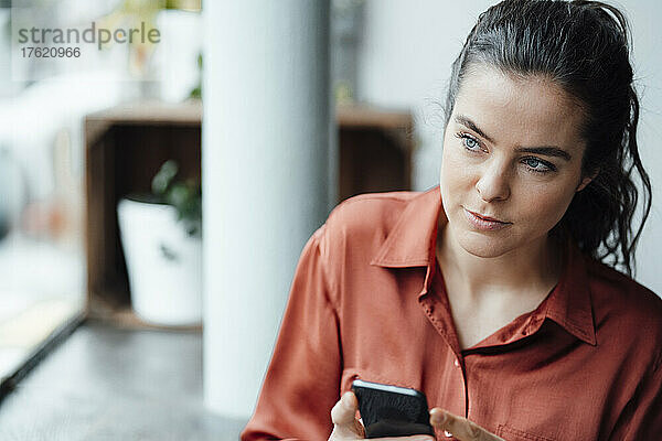 Contemplative woman with mobile phone in cafe
