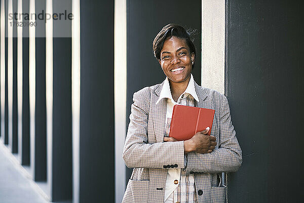 Happy businesswoman with tablet PC standing by wall
