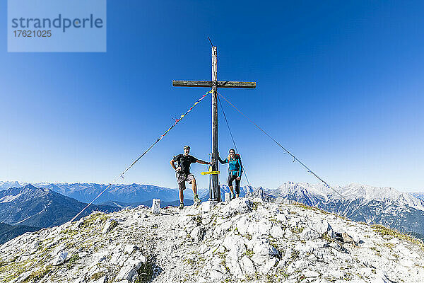 Zwei Wanderer posieren neben dem Gipfelkreuz der Brunnensteinspitze