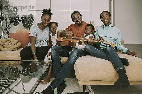Lächelnde Familie mit Gitarre sitzt auf der Couch