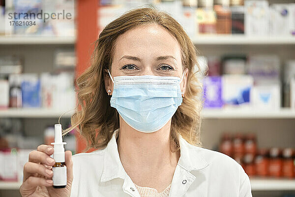 Apothekerin trägt eine schützende Gesichtsmaske und hält eine Flasche Nasenspray in der Apotheke