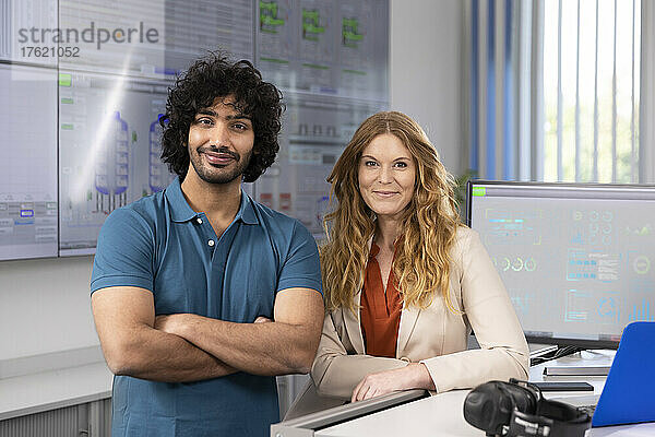 Lächelnde Geschäftsfrau mit Techniker am Schreibtisch im Kontrollraum