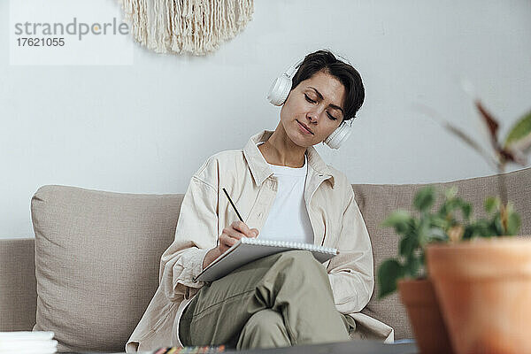 Künstler mit Kopfhörern skizziert auf Notizblock auf dem Sofa