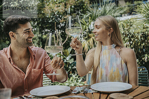 Lächelndes Paar prostet Weingläser am Tisch im Freien an