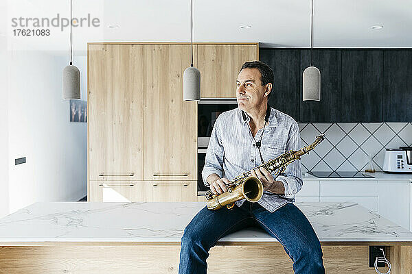 Saxophonist mit Saxophon sitzt zu Hause auf der Kücheninsel